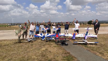 Groupe de personnes souriantes faisant signe, entourées de modèles réduits d'avions.